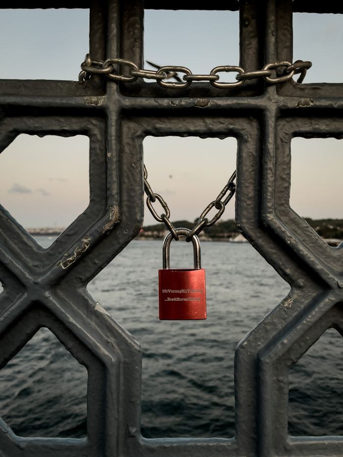 A red padlock linked with a chain on a fence over water in Istanbul, Türkiye.